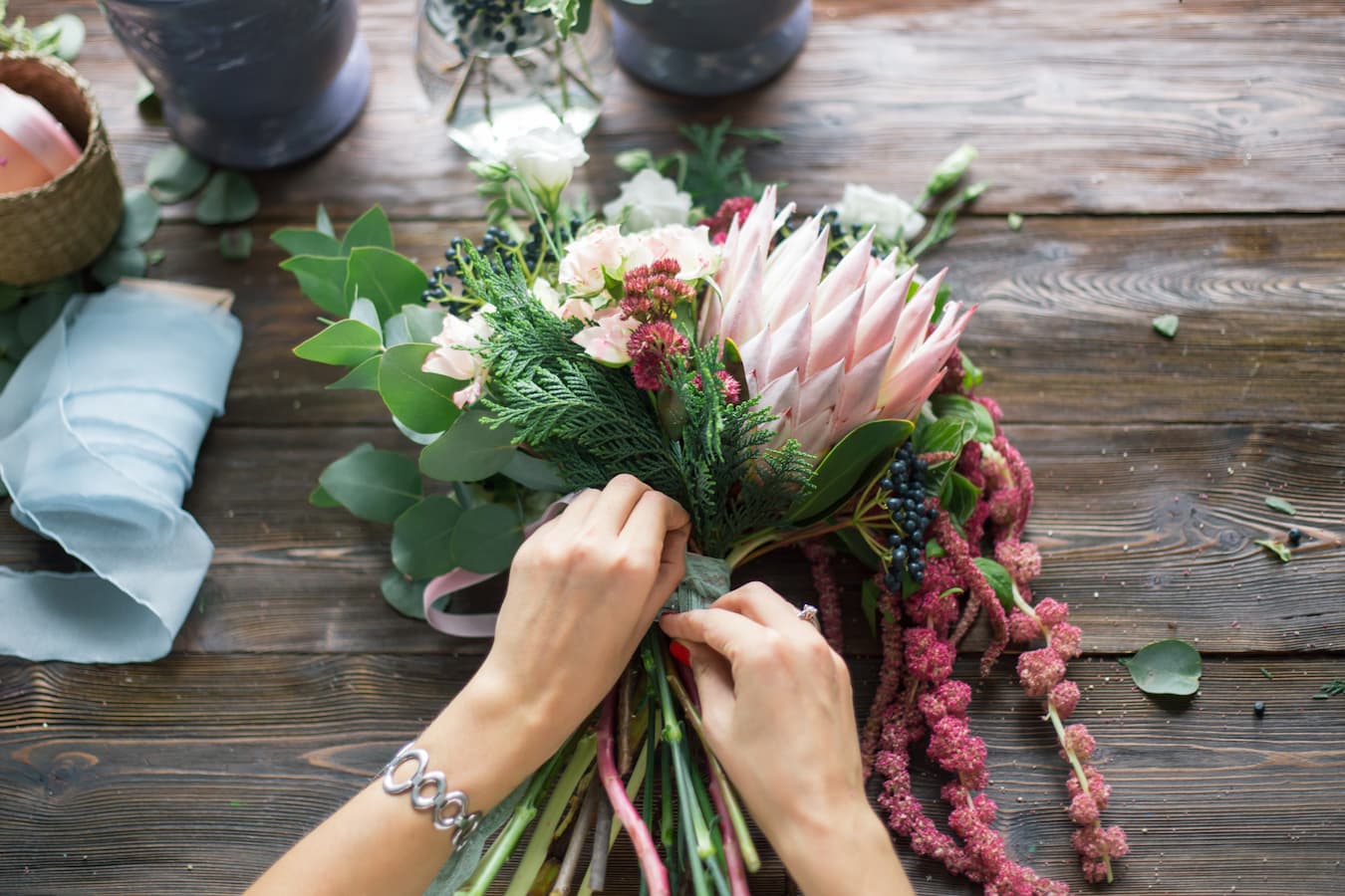 Floristin bindet Blumenstrauß mit Protea und Eukalyptus auf Holztisch